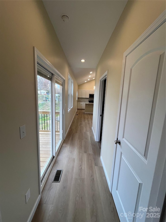 hallway featuring lofted ceiling, recessed lighting, visible vents, baseboards, and light wood-type flooring