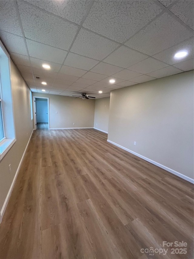 finished below grade area with a paneled ceiling, a ceiling fan, baseboards, and wood finished floors