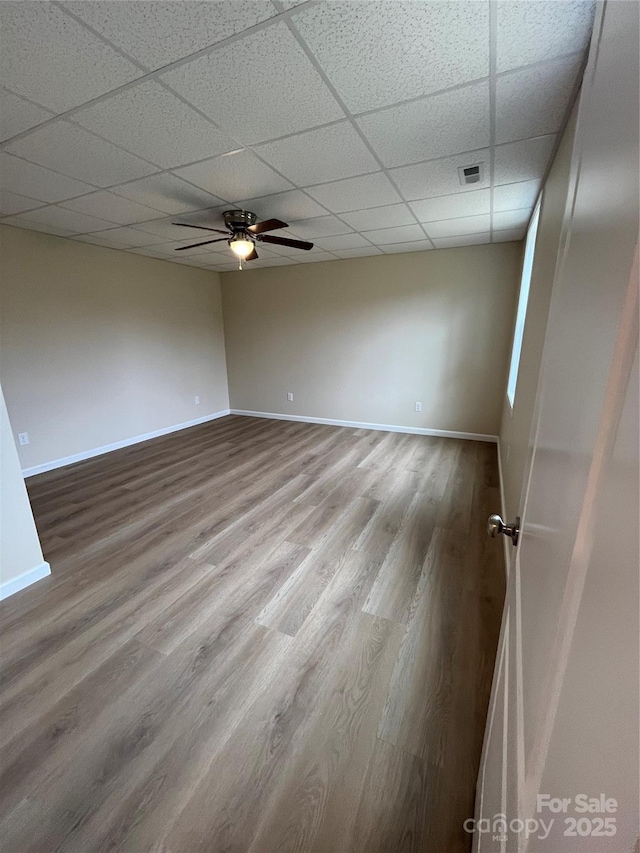 unfurnished room with ceiling fan, a paneled ceiling, wood finished floors, visible vents, and baseboards