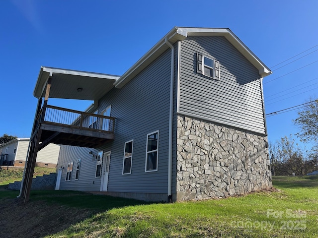 back of house with a balcony, stone siding, and a yard