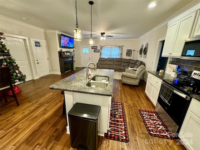 kitchen featuring stainless steel appliances, dark wood-type flooring, dark stone counters, sink, and an island with sink