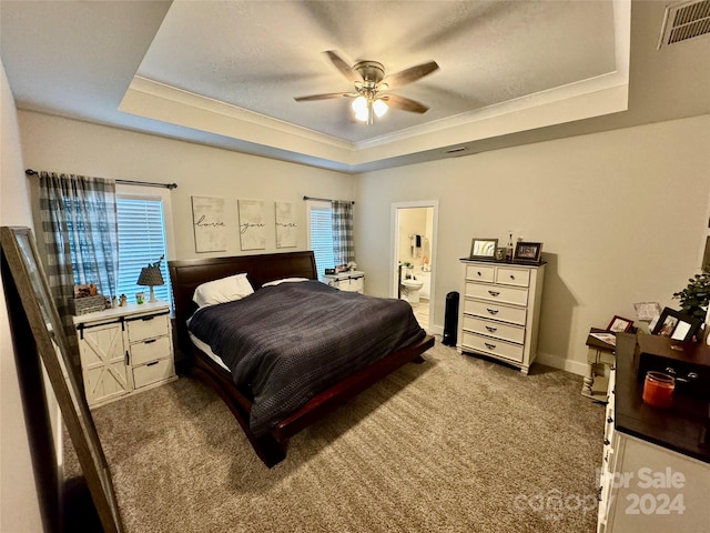 bedroom with ensuite bath, multiple windows, ceiling fan, and a tray ceiling