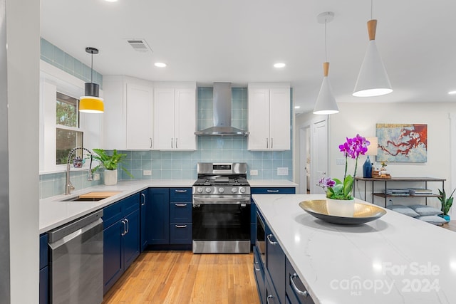 kitchen featuring white cabinetry, sink, wall chimney exhaust hood, hanging light fixtures, and appliances with stainless steel finishes