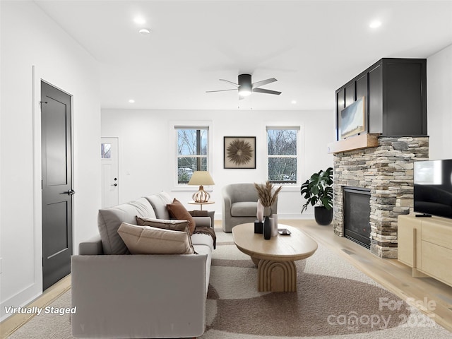 living room with a stone fireplace, recessed lighting, a ceiling fan, baseboards, and light wood finished floors