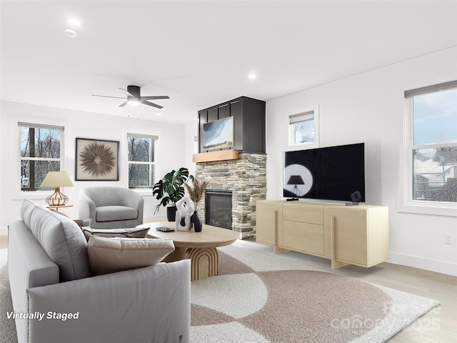 living area featuring baseboards, light wood-style flooring, ceiling fan, a stone fireplace, and recessed lighting