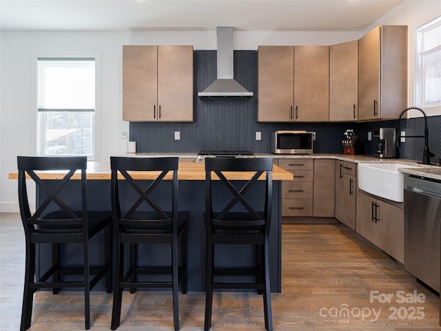 kitchen featuring stainless steel appliances, wall chimney range hood, a sink, and a breakfast bar