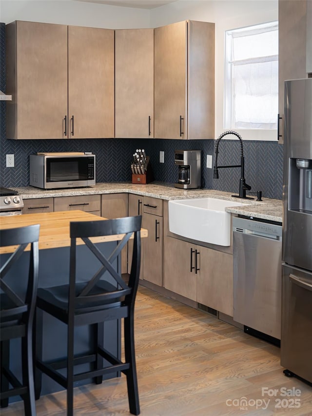 kitchen with light stone counters, decorative backsplash, appliances with stainless steel finishes, a sink, and light wood-type flooring