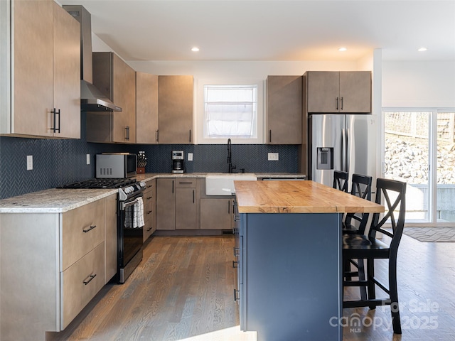 kitchen with a breakfast bar area, stainless steel appliances, a sink, a center island, and wall chimney exhaust hood