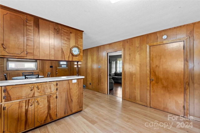 kitchen featuring wood walls, a textured ceiling, white microwave, and light wood-type flooring