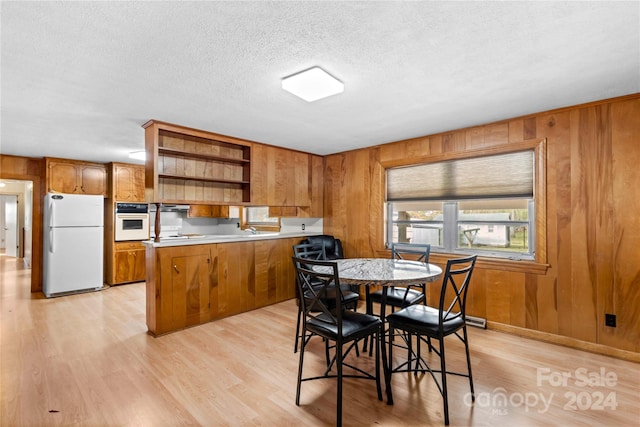 dining area featuring light wood-type flooring, wooden walls, and a textured ceiling