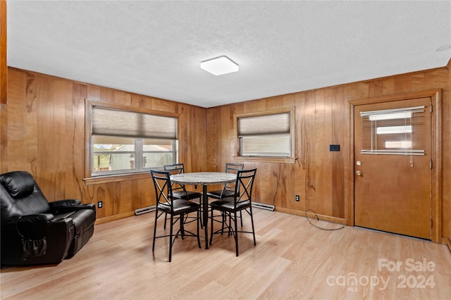 dining room featuring wooden walls, light wood-type flooring, and a textured ceiling