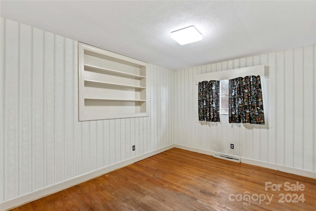 spare room featuring hardwood / wood-style floors, built in features, and a textured ceiling