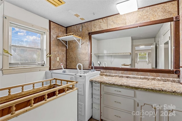 kitchen with a textured ceiling, washer / dryer, a healthy amount of sunlight, and white cabinets