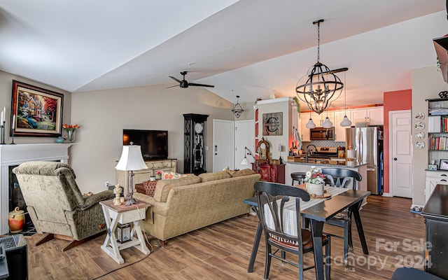 living room featuring ceiling fan with notable chandelier, lofted ceiling, sink, and wood-type flooring