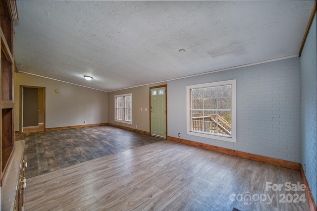 empty room featuring brick wall, wood-type flooring, a textured ceiling, and ornamental molding