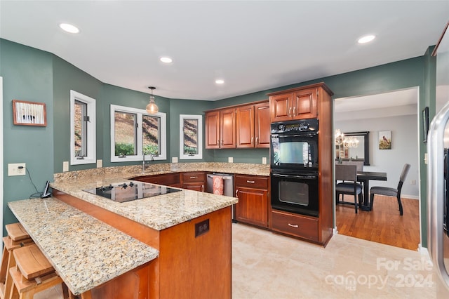 kitchen with kitchen peninsula, light stone countertops, a breakfast bar, black appliances, and hanging light fixtures