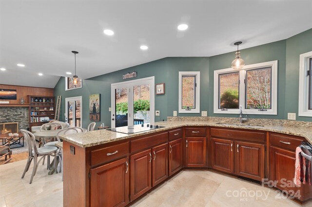 kitchen featuring sink, black electric stovetop, kitchen peninsula, pendant lighting, and a fireplace