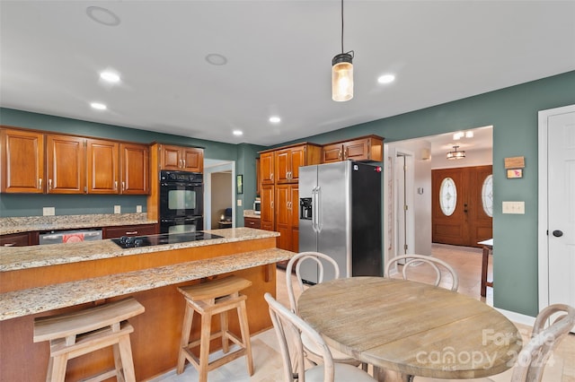 kitchen with black appliances, a kitchen breakfast bar, pendant lighting, and light stone counters