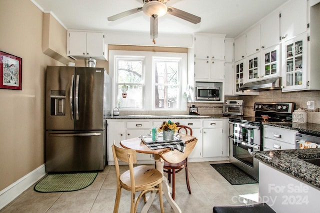 kitchen with stainless steel appliances, dark stone counters, light tile patterned floors, white cabinets, and decorative backsplash