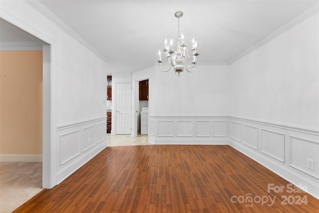 unfurnished dining area featuring ornamental molding, light wood-type flooring, a notable chandelier, and washer / dryer