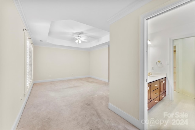 hallway featuring a raised ceiling, light colored carpet, and crown molding