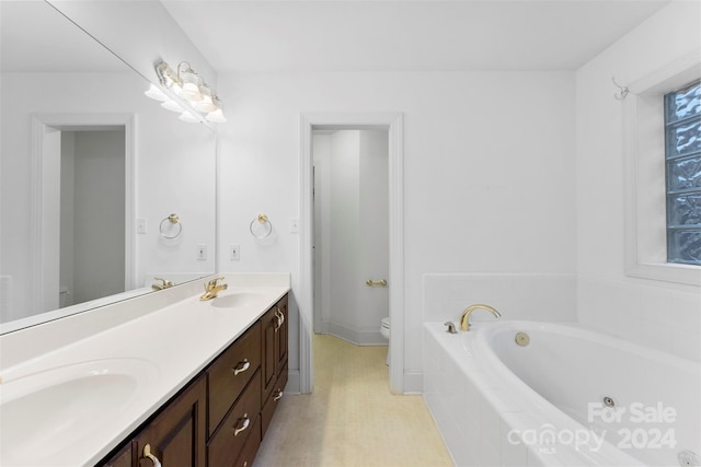 bathroom with vanity, tiled tub, and toilet