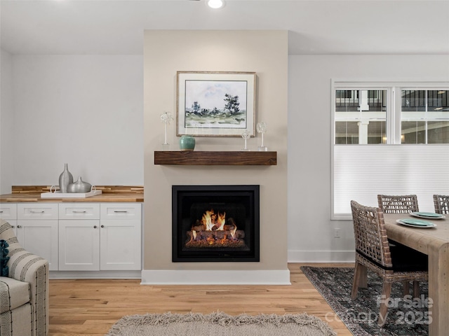 living area featuring baseboards, a lit fireplace, recessed lighting, and light wood-style floors