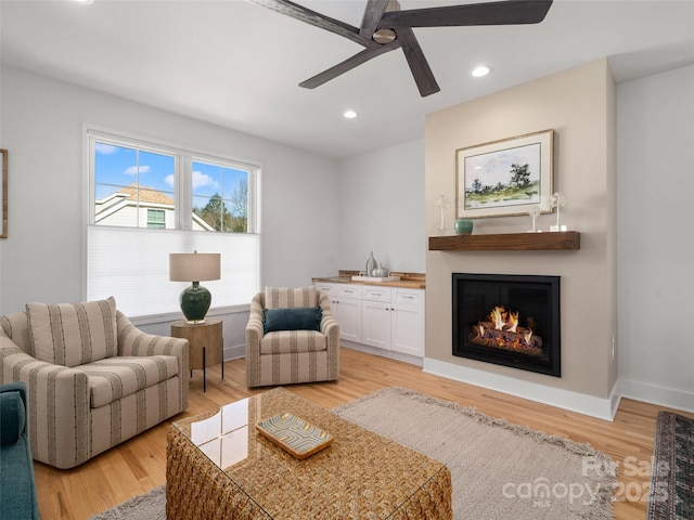 living area featuring recessed lighting, baseboards, ceiling fan, light wood-style flooring, and a glass covered fireplace