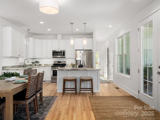 kitchen featuring recessed lighting, light wood-type flooring, a center island, white cabinets, and appliances with stainless steel finishes