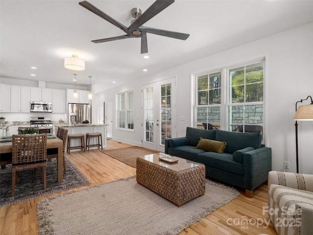 living area featuring baseboards, light wood-type flooring, ceiling fan, and recessed lighting