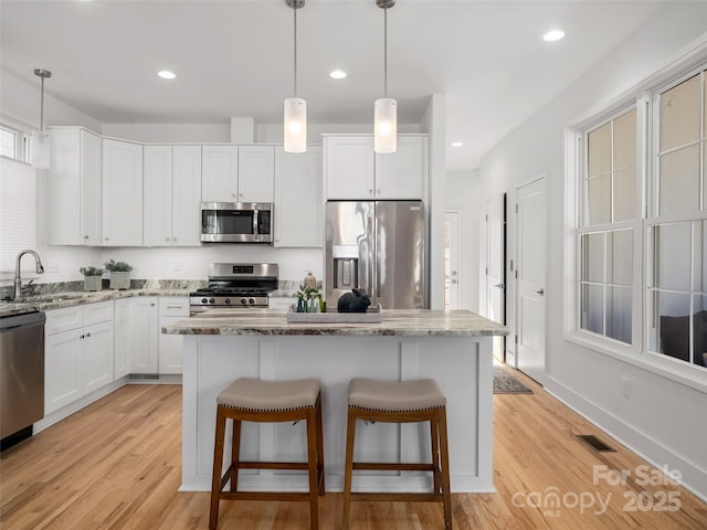 kitchen with white cabinets, light stone countertops, appliances with stainless steel finishes, a sink, and light wood-style floors
