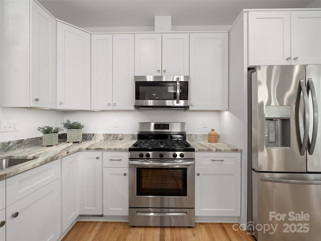 kitchen featuring white cabinets, appliances with stainless steel finishes, light wood-style floors, and light stone counters