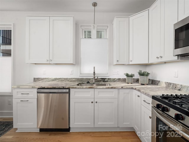 kitchen with light stone counters, a sink, light wood finished floors, appliances with stainless steel finishes, and white cabinets