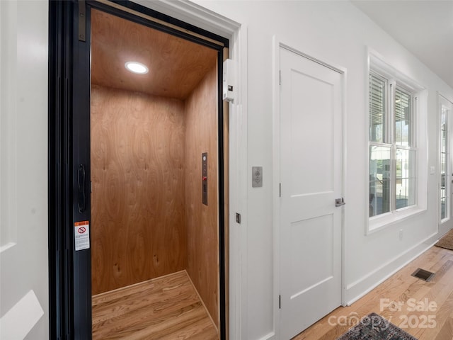 room details with wood finished floors, elevator, baseboards, and visible vents