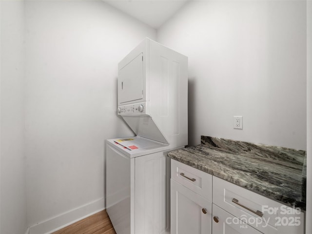 clothes washing area featuring light wood-style floors, cabinet space, baseboards, and stacked washing maching and dryer
