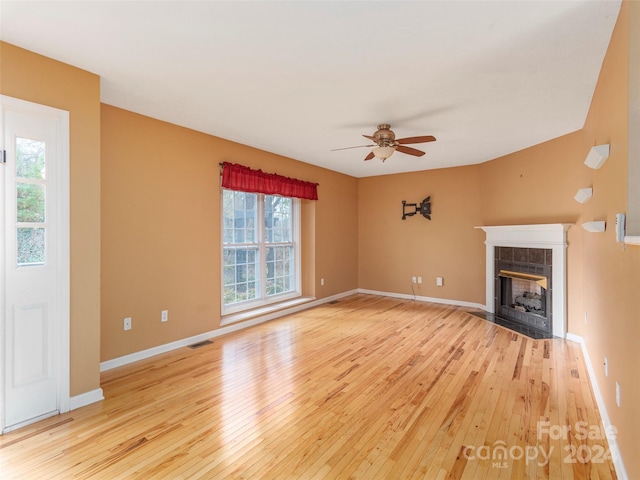 unfurnished living room featuring ceiling fan, a tiled fireplace, and light hardwood / wood-style floors