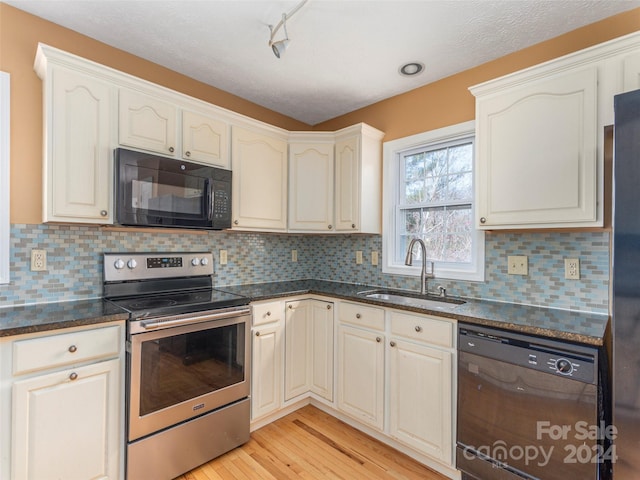 kitchen featuring sink, dark stone countertops, tasteful backsplash, black appliances, and light hardwood / wood-style floors