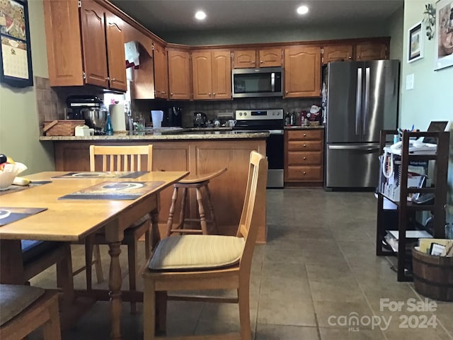 kitchen featuring backsplash, kitchen peninsula, a kitchen bar, and stainless steel appliances