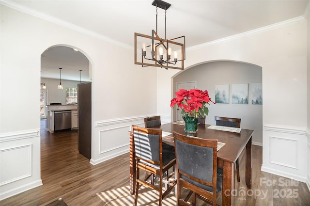 dining space with dark wood-type flooring, ornamental molding, and an inviting chandelier