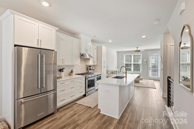 kitchen with a center island with sink, sink, white cabinetry, light stone counters, and premium appliances