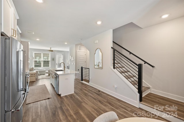 kitchen with stainless steel appliances, white cabinetry, sink, an island with sink, and dark wood-type flooring