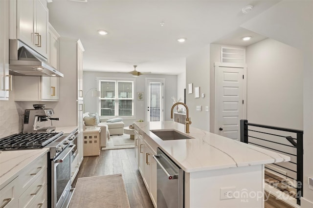 kitchen with hardwood / wood-style floors, sink, an island with sink, extractor fan, and appliances with stainless steel finishes