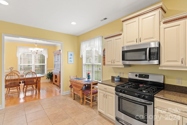 kitchen with appliances with stainless steel finishes, light hardwood / wood-style floors, cream cabinetry, and an inviting chandelier