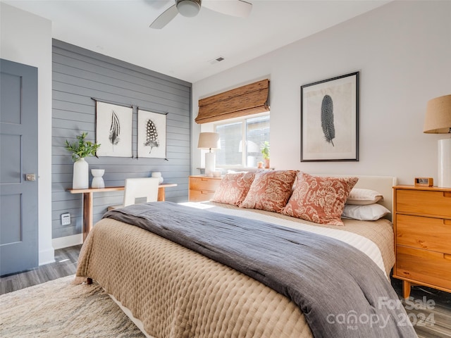 bedroom featuring dark hardwood / wood-style flooring, ceiling fan, and wooden walls