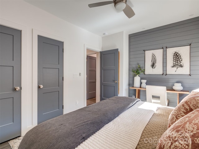 bedroom featuring ceiling fan and wooden walls