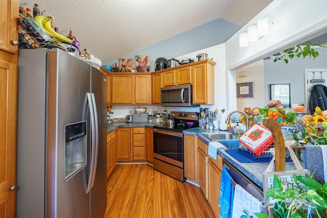 kitchen featuring sink, stainless steel appliances, light hardwood / wood-style flooring, a textured ceiling, and lofted ceiling