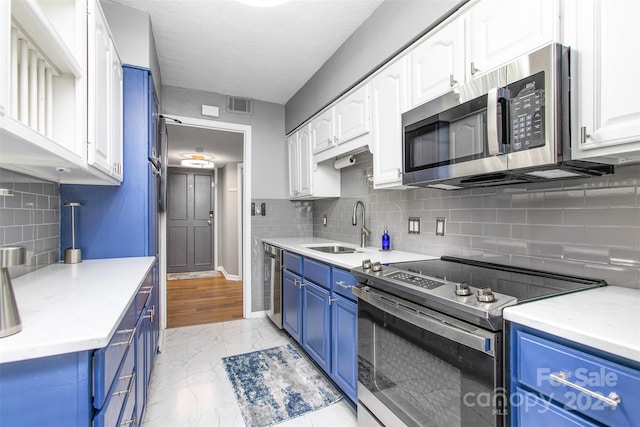 kitchen featuring blue cabinets, white cabinets, decorative backsplash, sink, and appliances with stainless steel finishes