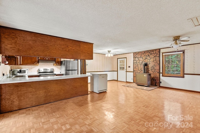 kitchen with a wood stove, a textured ceiling, kitchen peninsula, stainless steel appliances, and light parquet flooring