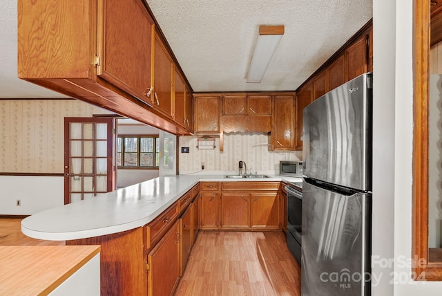 kitchen featuring sink, a textured ceiling, appliances with stainless steel finishes, light hardwood / wood-style floors, and kitchen peninsula