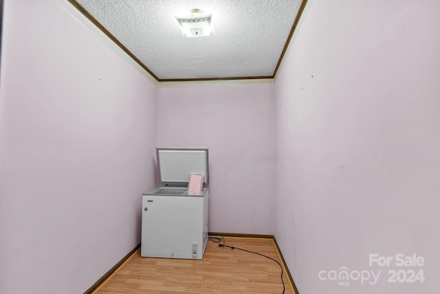 laundry area featuring a textured ceiling, light wood-type flooring, and ornamental molding